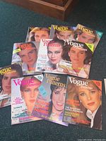 A layout of eleven vintage Vogue Pattern magazines spread on a carpet showing various cover designs and text related to sewing patterns and vintage fashion.