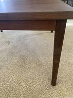 Close-up of one tapered removable leg attached to the wood coffee table showing wood grain and minimalist design.