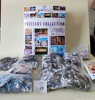 Photo showing 8 unopened bags of puzzle pieces laid out on table with the puzzle box behind them.