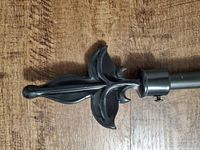 Close-up of one decorative fleur-de-lis finial on the black curtain rod showing details of the design and metal finish.