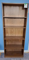 Front view of a tall, narrow wooden bookshelf with four shelves.