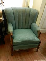 Front view of the highback armchair showing textured green upholstery and carved wooden arms and legs.