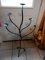 Full view of the large black metal 5-branch candle holder with round candle platforms and tripod legs.