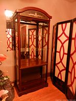 Full view of the tall wood and glass display cabinet with mirrored back, glass shelves, and wooden bottom shelf. Shows reflective interior and outer wood frame.