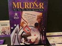 Photo showing the Murder à la Carte mystery party game box with decorated cover and some invitation cards.