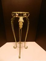 Front view of ornate green metal plant stand with leaf motif and glass accents around top ring.