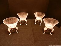 Four clear crackle glass and metal candle holders arranged in a row on a dark fabric background showing glass bowls and metal bases.