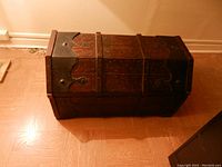 Top-front and side view of wooden trunk showing metal decorative accents and rivets.