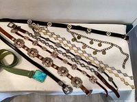 Full spread of all vintage belts showing various styles: chain link, leather with large silver western buckles, braided, and suede with art glass buckle.