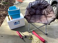 White Huskee 48-can cooler with smaller blue plastic cooler on top, brown padded folding chair, yellow flashlight, orange lantern, red tent bag, black tent poles and yellow tent stakes with yellow rope.