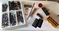 Full overview of assorted drill bits, hole saws, and driver bits arranged in trays and boxes on a table.