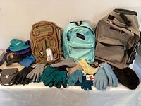 Full lot showing backpacks, gloves, hats, and handbag arranged on a table and against a wall.