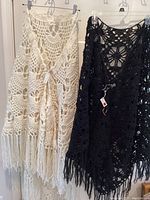 Two hand crocheted shawls hanging, one cream colored and one black, both with fringe