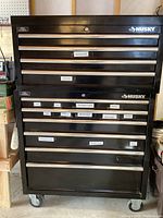 Full front view of black Husky tool cabinet showing top chest and base cabinet on casters