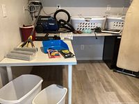 Wide view of laundry and cleaning supplies including vacuum, mop, baskets, trash cans, and ironing board