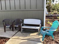 Full view of the set showing the green Adirondack chair, two brown stacking chairs, and the white gliding bench outside on a concrete patio.
