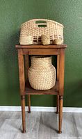 Planter stand with large woven vase-shaped basket on lower shelf and three small woven baskets on top surface