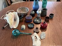 Overview of all items on wooden table including seashell lamp, pottery, glass and stone pieces.