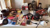 Table with RIDGID belt sander, orbital hand sander, sanding belts, sandpaper packs, steel wool, ear protection, goggles.