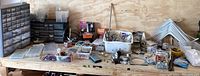 Overview of entire workspace showing multiple containers, organizers, and hardware spread out on a wooden bench.