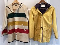 Front view of Woolrich striped wool jacket and yellow rain slicker jacket on hangers showing color, hood, and pocket details.
