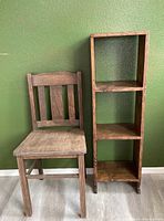 Photo showing the wooden chair and the wooden shelf side by side against a green wall on a wood floor.