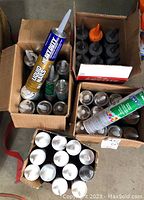 Photo showing four boxes filled with various tubes of adhesives and sealants including Liquid Nails and Mapai adhesive cartridges.