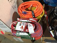 Multiple coiled extension cords in orange, white/red striped, and yellow, stacked together showing unused, with packaging tags visible.