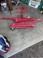 Red steel panel hoist components laid out on a concrete floor, including frame segments and legs