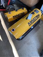 Two yellow cylindrical Master kerosene heaters placed on a concrete floor, showing their size and branding.