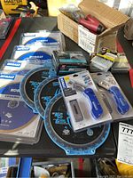 Photo showing Kobalt ceramic tile blades in packaging, Spyder tarantula saw blades, Kobalt folding carpet cutters in blue plastic blister packs, and a cardboard box with red-handled notched trowels and nails.