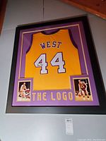 Full frontal view of framed Lakers jersey on wall showing jersey, mat, frame, photos and THE LOGO text