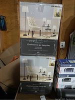 Two boxed Charlestown Signature Series 4-piece lamp sets stacked in a garage area, with original packaging showing product image and details.
