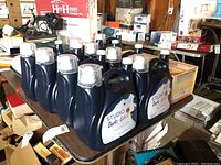 Nine dark blue Tide Studio Darks + Colors detergent bottles on a table in a garage setting