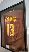 Framed brown San Diego Padres jersey with the name Machado and number 13 in yellow and white stitched lettering inside a black frame.