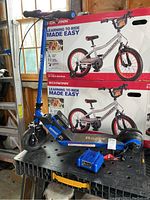 Blue Kobalt Razor scooter on black surface near window, background boxes of Schwinn bicycles.