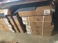 Stacked tightly packed cardboard boxes containing adhesive rug tiles.