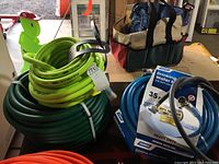 Overview of multiple water hoses including neon Flexzilla hose, green hose, and blue drinking water-safe hose with packaging visible.