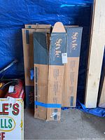 Five boxes of Style Selections wood tongue and groove flooring stacked on a garage floor with blue tarp background.