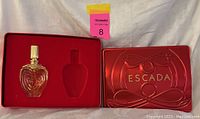 Full gold-tone ornate ESCADA perfume bottle in red metal ESCADA case with cutout insert for the bottle shape.