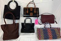 Lot of six ladies purses arranged on white backdrop showing overall variety, colors, and designs.