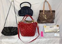 View showing five purses: light tan Monsac tote, black Marco Avane purse, Sylvia black purse, bright red Bracciano patent leather purse, and large silver Charles David clutch with gold corners and wrist strap