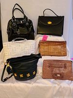 Group photo showing six purses including the black leather briefcase, black patent bowler, white woven handbag, brown embossed clutches, and black bucket bag.