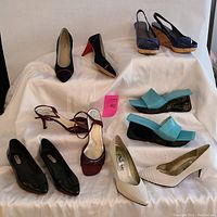 Six pairs of ladies shoes displayed on white cloth, showing different styles including wedge platforms, slingbacks, and closed pumps in various colors.