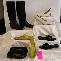Full view of all five pairs of ladies' shoes arranged on white fabric background, including boots, pumps, flats, and slides in black, beige, and green.