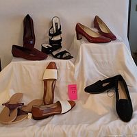 Full view of all six pairs of ladies shoes arranged on fabric-covered steps showing variety in colors, styles, and brands including pumps, slides, loafers, and sandals.