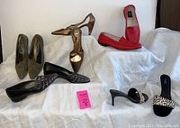All five pairs of shoes displayed on white cloth and steps showing various styles and colors including red loafers, olive flats, animal print heels, and black flats.
