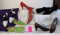 Five pairs of women's shoes displayed on white fabric including brown heels, coral/red heels, black suede flats, green slip-ons, and white Yves Saint Laurent flats.