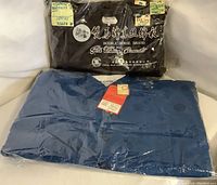 Two jackets sealed in original plastic packaging; one black, one blue. Brand and silk content tags visible.
