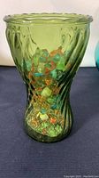 Side view of green glass vase filled with multicolored marbles including green, orange, and blue shades, with swirl glass texture visible